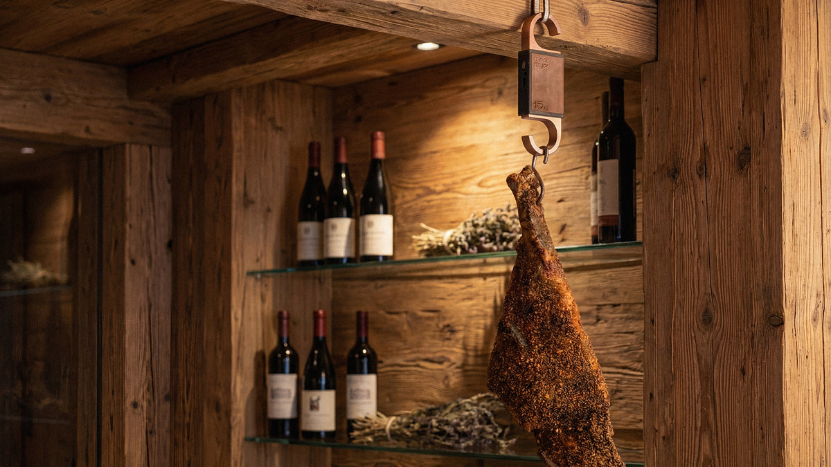Wine bottles on shelves in a rustic wooden room with cured meats, prosciutto, serrano